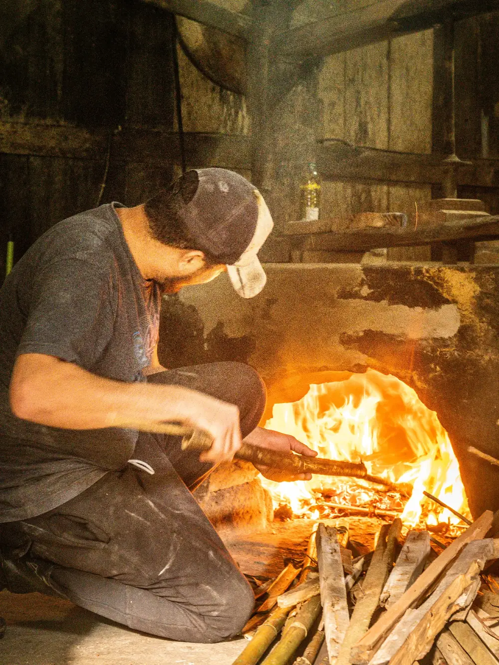 Homem alimentando o fogo da fornalha de um alambique tradicional
