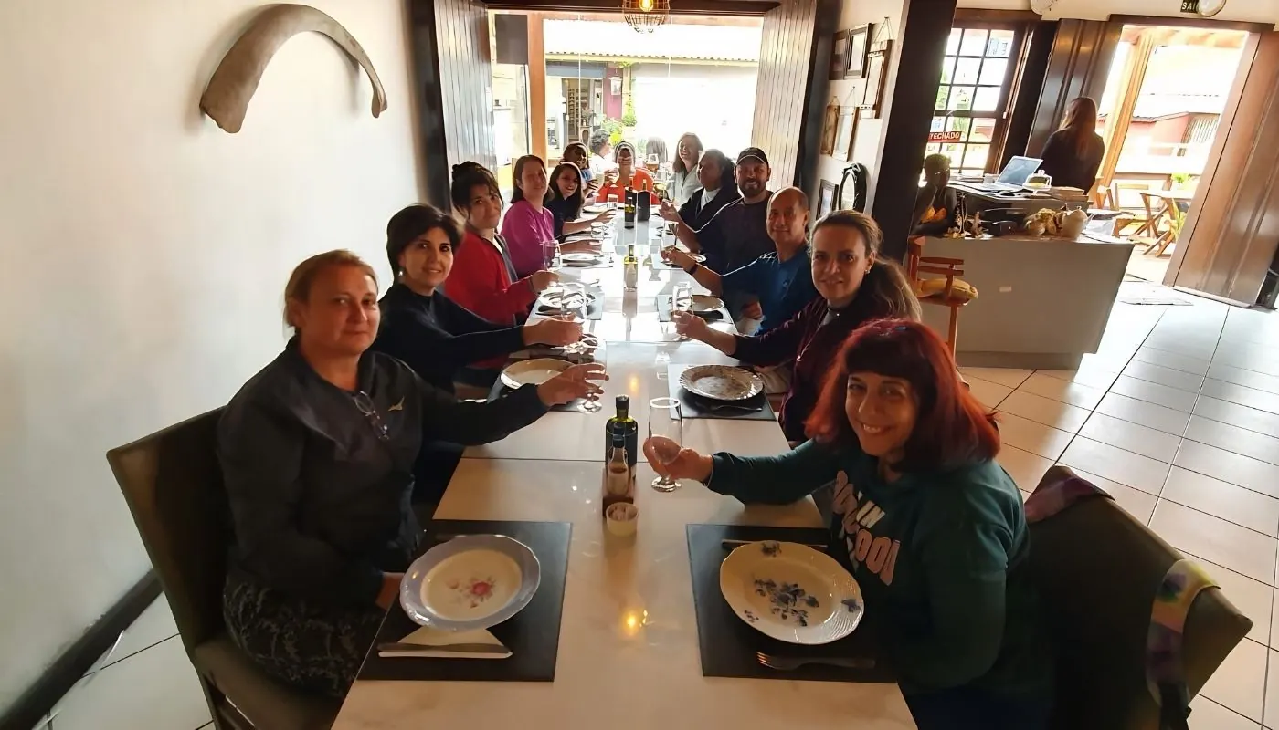 Grupo reunido em uma mesa comprida de restaurante, brindando com taças