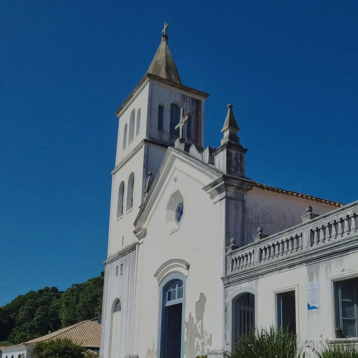 Torre e fachada branca da igreja matriz de Garopaba contra o céu azul