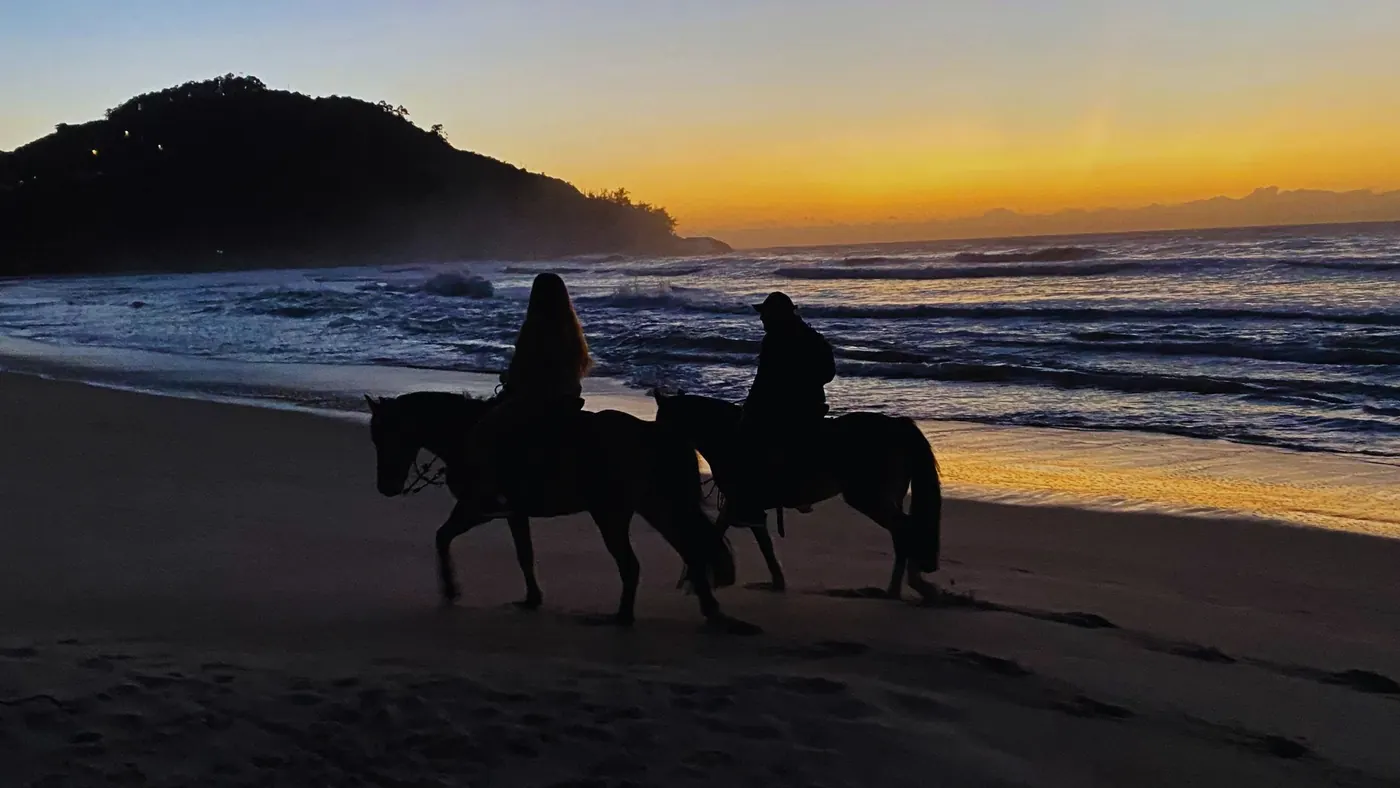 Duas pessoas a cavalo na praia ao pôr do sol