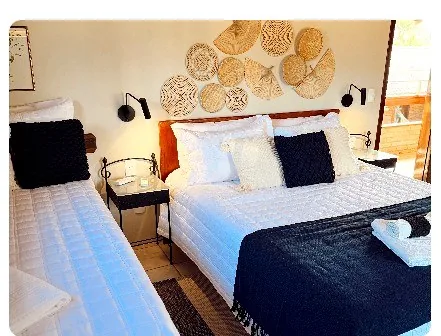 Quarto com cama de casal, cama de solteiro e painel de palha na parede